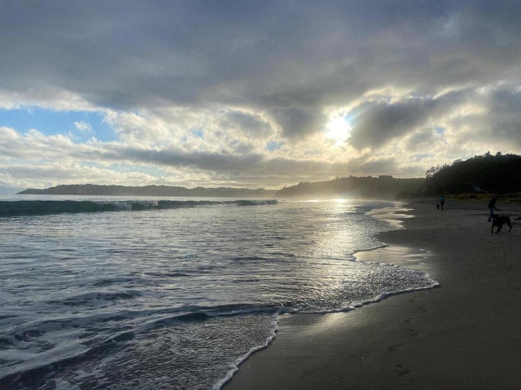 a beach with people walking on the sand and the water at Casita Vista Waiheke in Waiheke Island