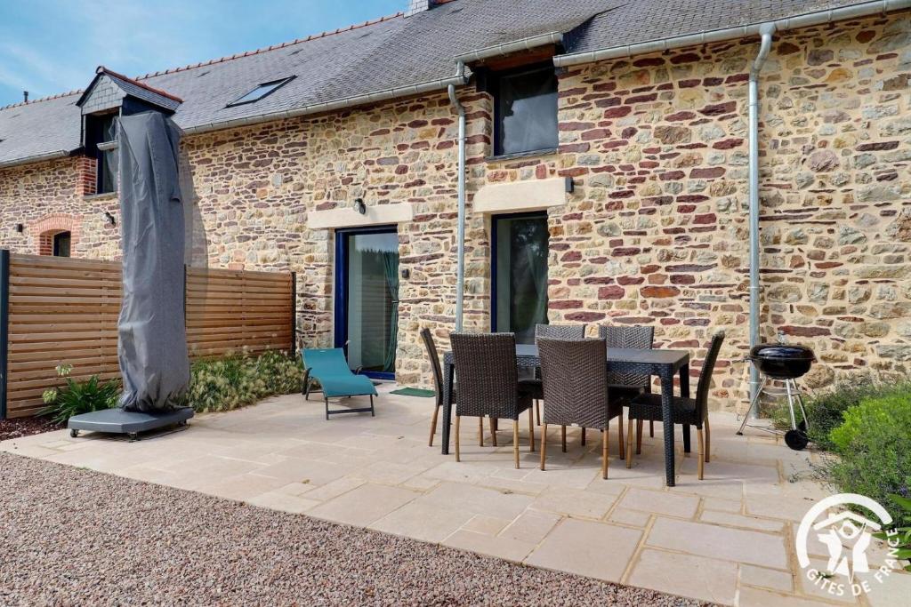 a patio with a table and chairs in front of a brick building at Le refuge enchante in Paimpont
