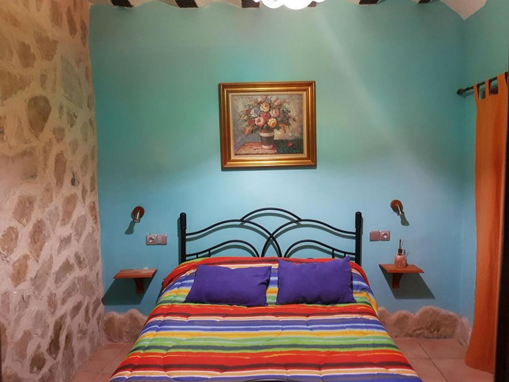 1 dormitorio con 1 cama con una pintura en la pared en Casa Rural Valle del Cabriel en Enguídanos
