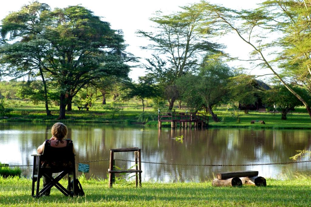 a woman sitting in a chair in front of a lake at Voyager Ziwani Tented Camp in Ziwani