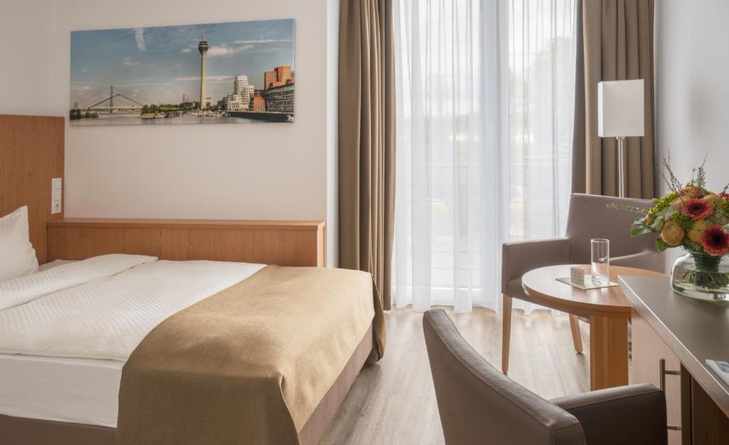 デュッセルドルフにあるHotel Chrismaのベッド、デスク、椅子が備わるホテルルームです。