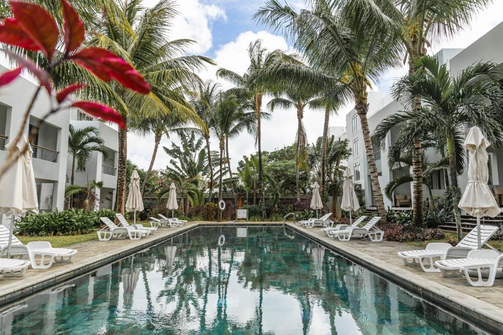 a swimming pool with chaise lounge chairs and palm trees at La Residence Sea Horse and Seashell Beachfront Apartment 23 in Cap Malheureux