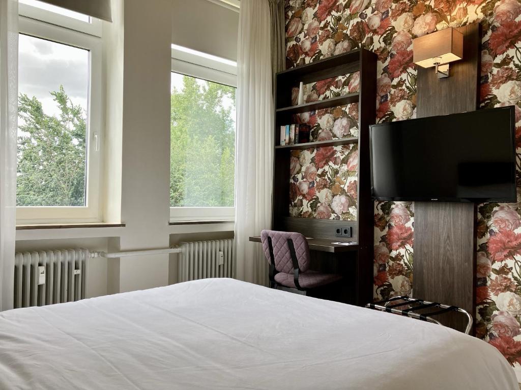 a bedroom with a bed and a tv and windows at Fährhaus Hotel am Rhein by Mayburgh in Düsseldorf