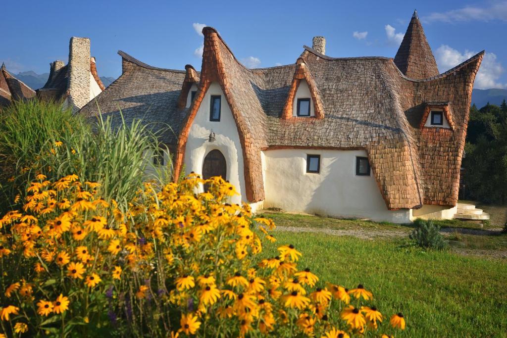 a house with a roof with yellow flowers in the foreground at Castelul de Lut - Eco Boutique Guesthouse in Porumbacu de Sus