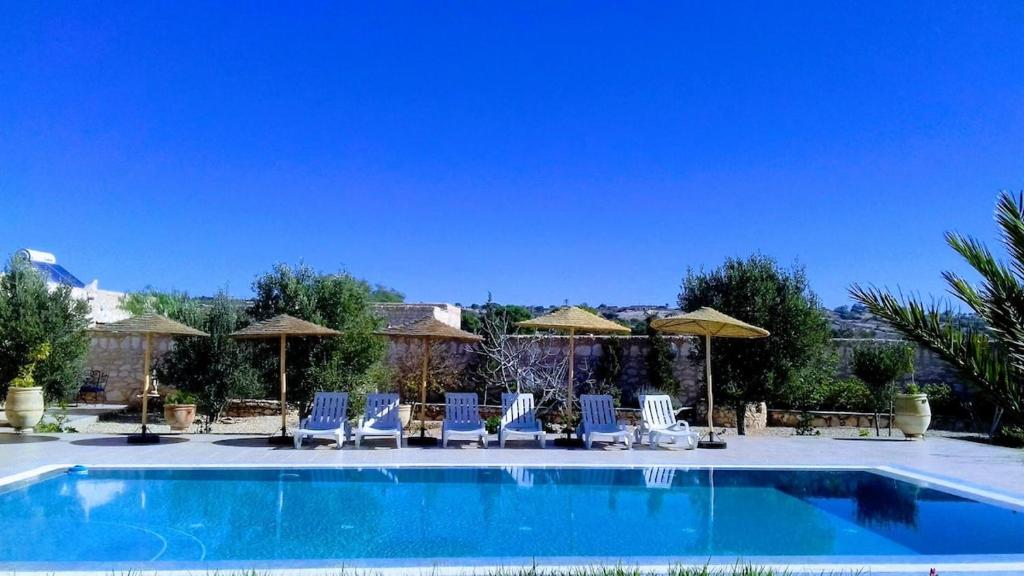 a swimming pool with chairs and umbrellas at Villa Dar Albatros Great for groups surf, yoga, friends and family in Sidi Kouaki