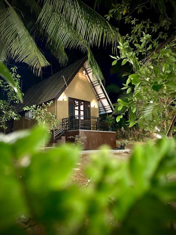 a small house is seen through the leaves of trees at Sansun Villa in Harumalgoda West