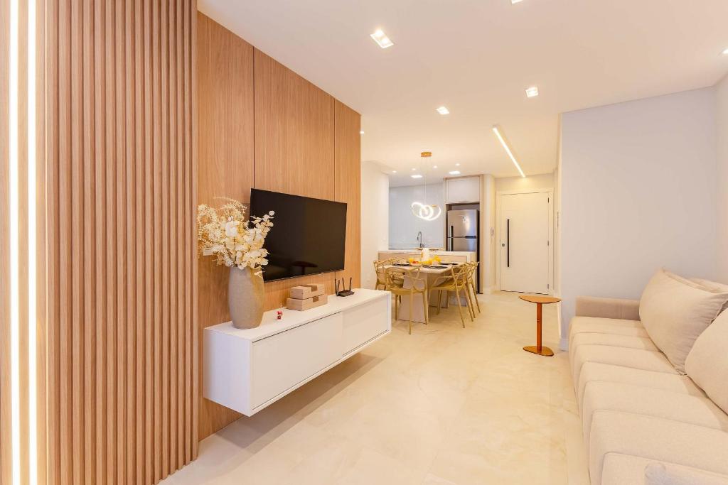 a living room with a white couch and a tv at Belissimo apto alto padrão a 50 mts da praia in Bombas