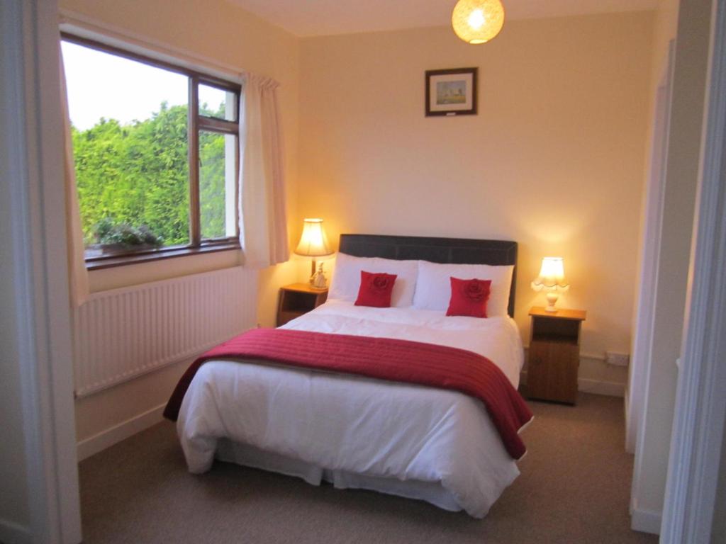 a bedroom with a bed with red pillows and a window at Greenfields Farmhouse in Ballylongford
