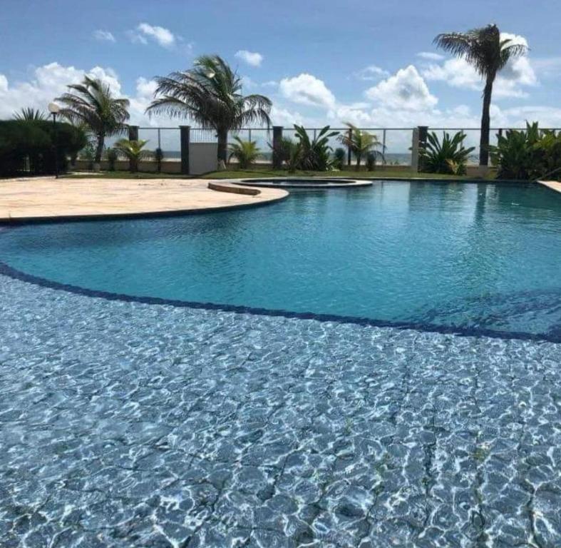 a swimming pool with blue water and palm trees at Apartamento - Garden Flat Mar Azul in Taíba