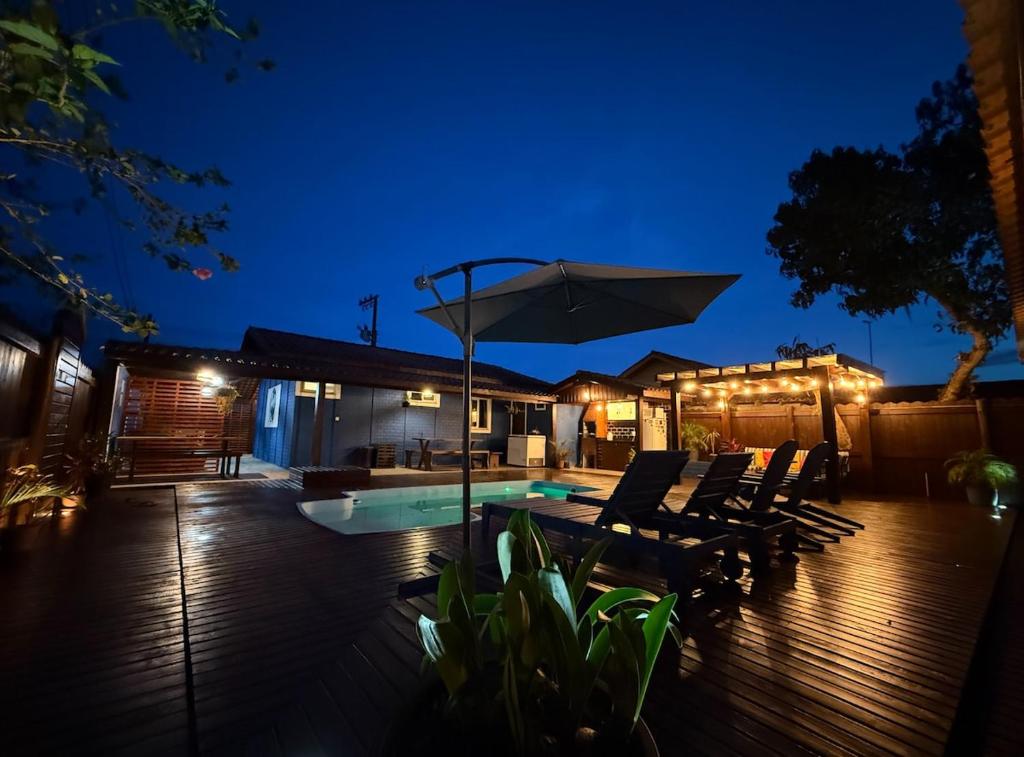 a patio with chairs and an umbrella at night at Inn Nature Pousada Casa de Veraneio com piscina in Palhoça