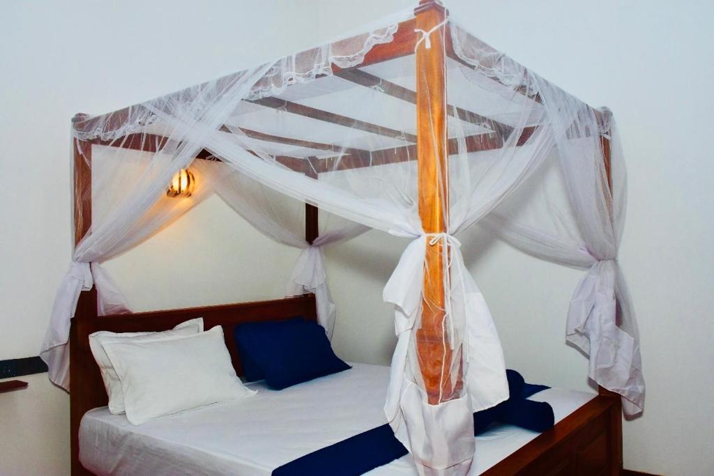 a bedroom with a canopy bed with blue pillows at Yala Grand Homestay in Tissamaharama