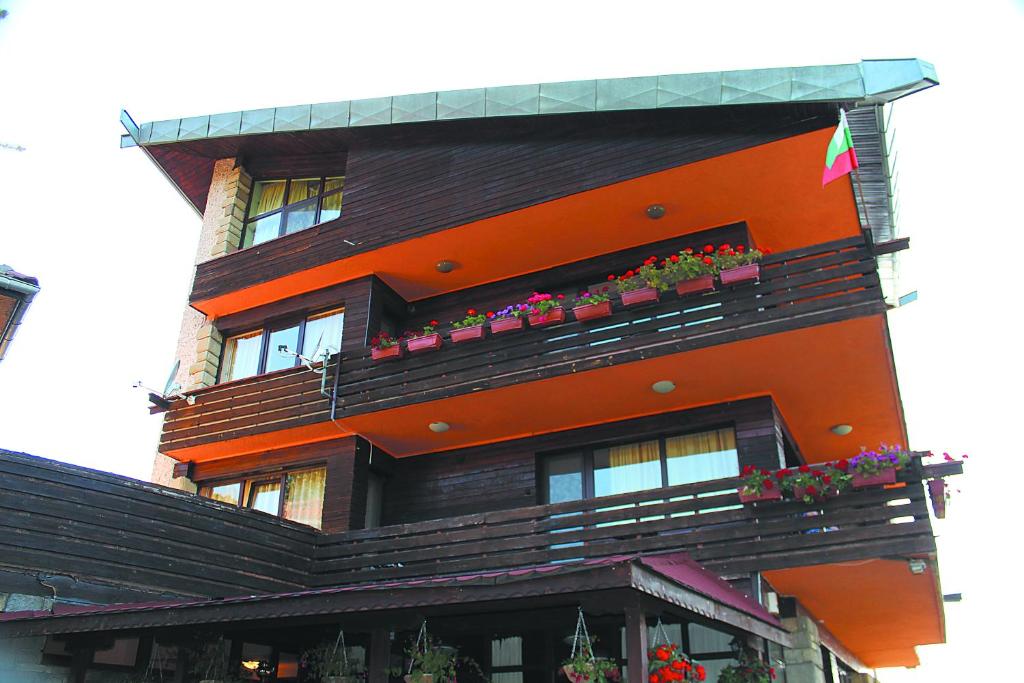an orange building with potted plants on the balconies at Guest House Daskalov in Chervena Lokva