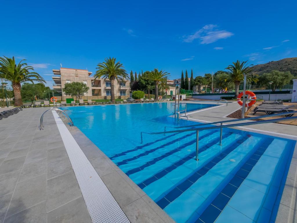 a large swimming pool with blue water and palm trees at Agi Rescator Apartments in Roses
