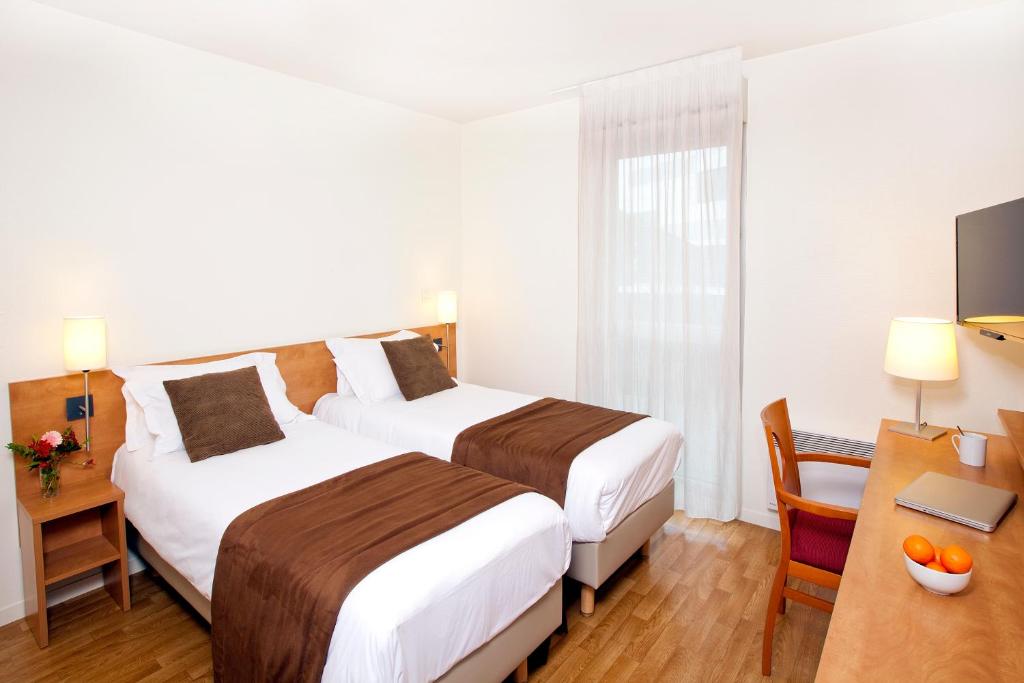 レンヌにあるSéjours & Affaires Rennes Longs Champsのベッド2台とデスクが備わるホテルルームです。