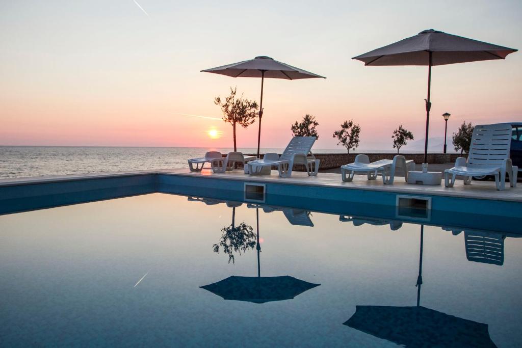 a swimming pool with chairs and umbrellas and the ocean at Apartments Harmony in Utjeha