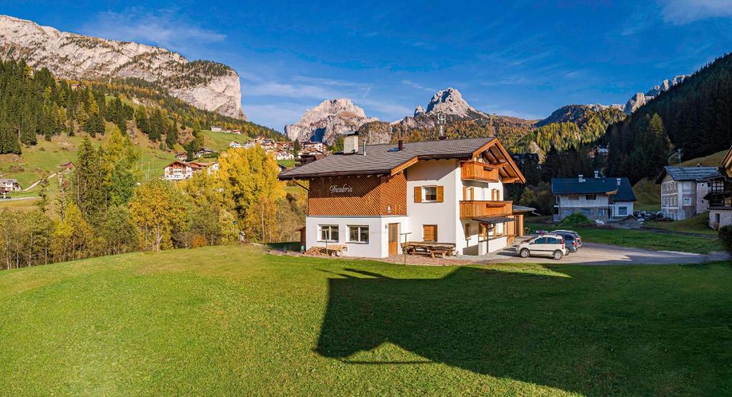 a house on a green field with mountains in the background at Dumbria Dolomites in Selva di Val Gardena