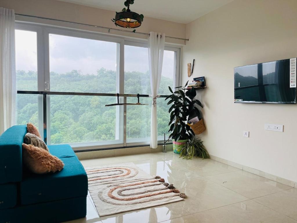 Una sala de estar con un sofá azul y una ventana grande. en Casa Symphony- Hill View Spacious Studio in Baner-Pashan, en Pune