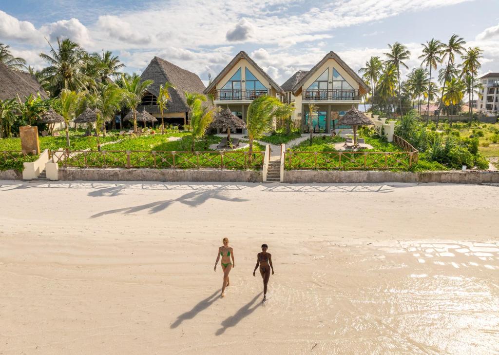 two people walking on the beach in front of a resort at Clove Island Essence & Spa Boutique in Matemwe