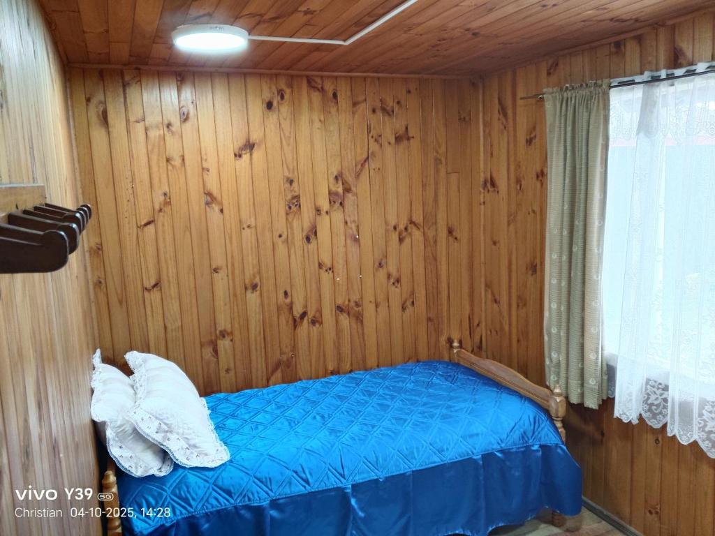 um quarto com uma cama azul numa parede de madeira em Hospedaje Mirador del Puerto em Quellón