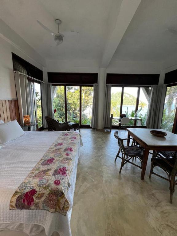 a bedroom with a bed and a table and windows at Vista para o Mar - Studio com 2 banheiros - Barra do Sahy in São Sebastião