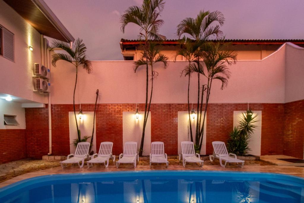 een zwembad met witte stoelen en palmbomen bij Nana Suites in Foz do Iguaçu