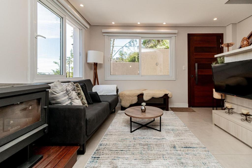 a living room with a black couch and a tv at Casa Paris em condomínio até 8 p in Canela