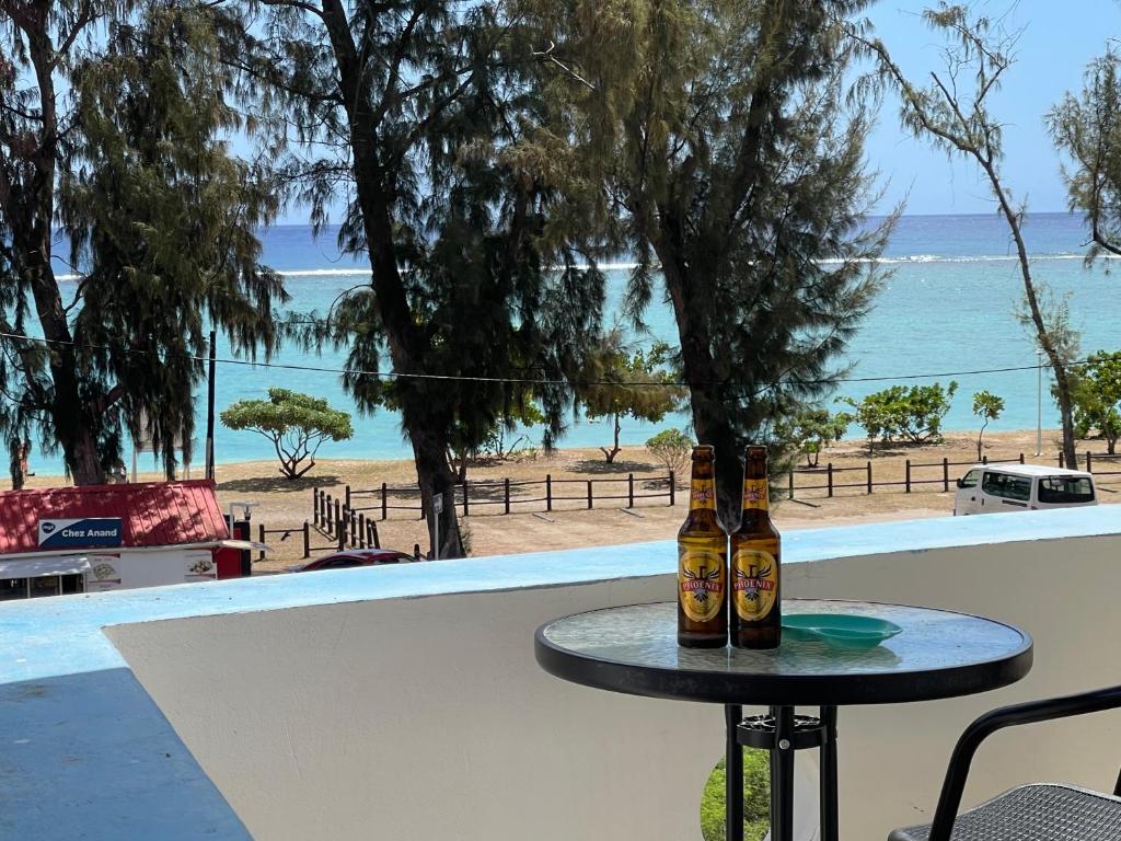 two bottles of beer sitting on a table in front of a beach at Spacious 3 bed seaview apartment in Flic-en-Flac