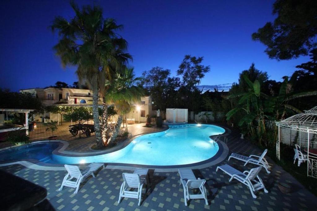 a pool with chairs and a palm tree at night at Regent Beachotel in Reggio Calabria