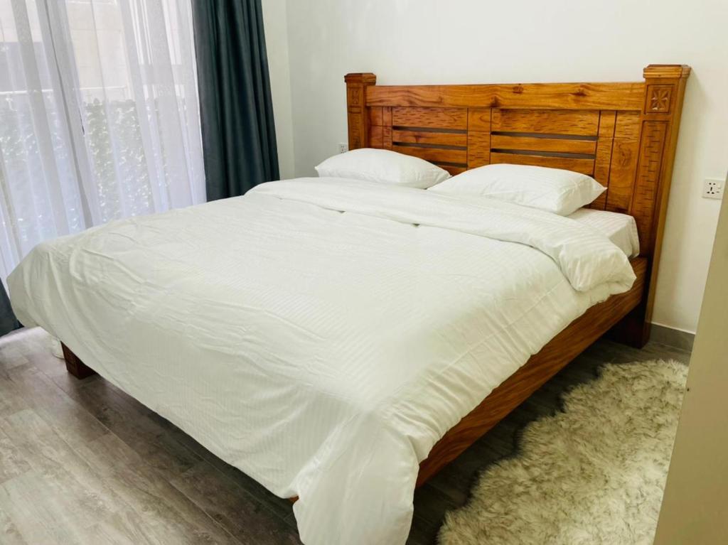 Elle comprend un grand lit avec des draps et des oreillers blancs. dans l'établissement Newrise Gardens Apartments, à Nairobi