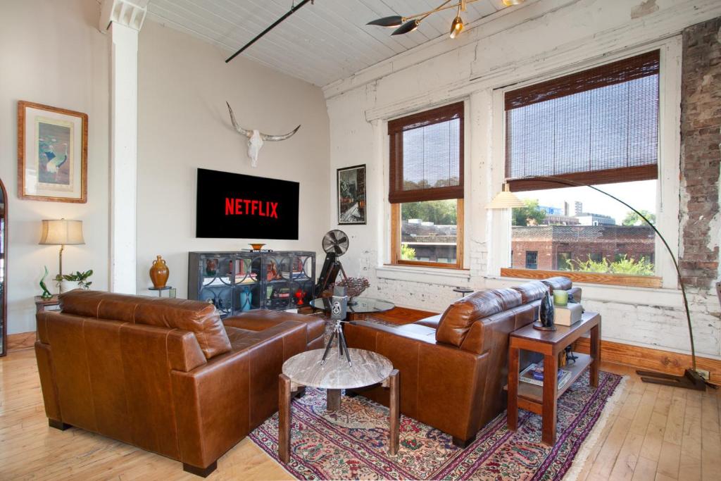 een woonkamer met een bruine leren bank en een tv bij Urban Haven Loft Near Market Square in Knoxville