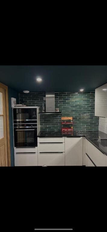 a kitchen with white cabinets and green tile on the wall at Le gîte de capucine in Saint Loup Lamaire