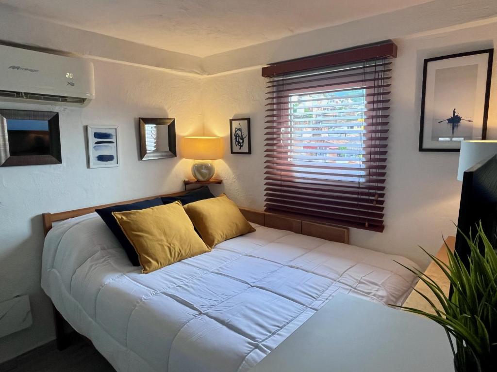 a bed with yellow pillows in a room with a window at Petit Bonheur - Calm Intimate - Terrace & Beach in Puerto Vallarta