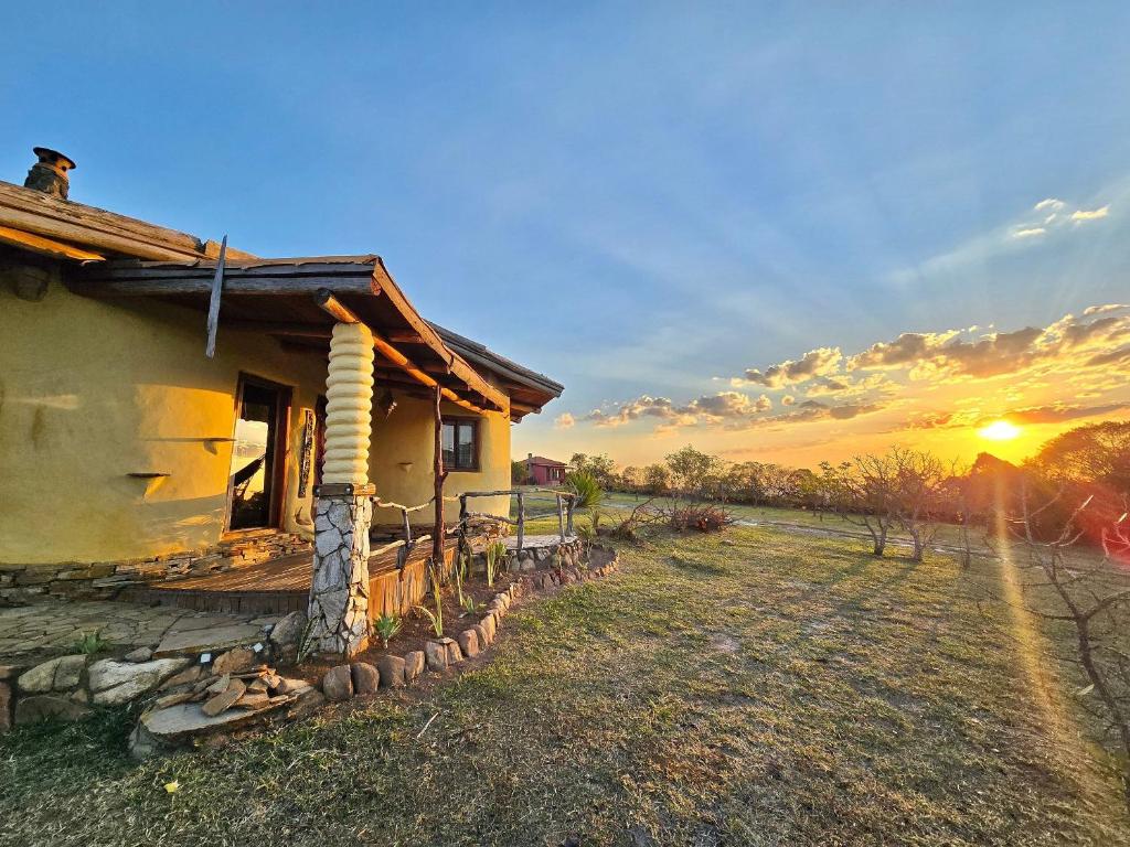 a house in a field with the sunset in the background at Chalés Vila Carrancas - Unidade Serra in Carrancas