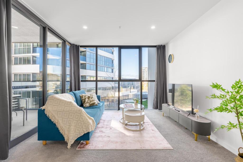 a living room with a blue couch and large windows at Stylish Woden Apt Near Hospital w Pool, Parking in Phillip