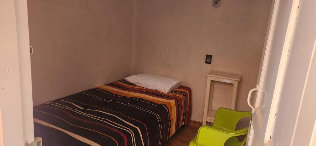 ein kleines Schlafzimmer mit einem Bett und einem grünen Stuhl in der Unterkunft El Jacalito in Matehuala