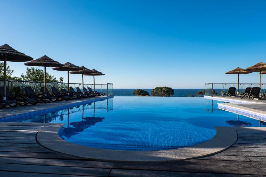 a swimming pool with chairs and umbrellas and the ocean at Vila Alba Resort in Carvoeiro