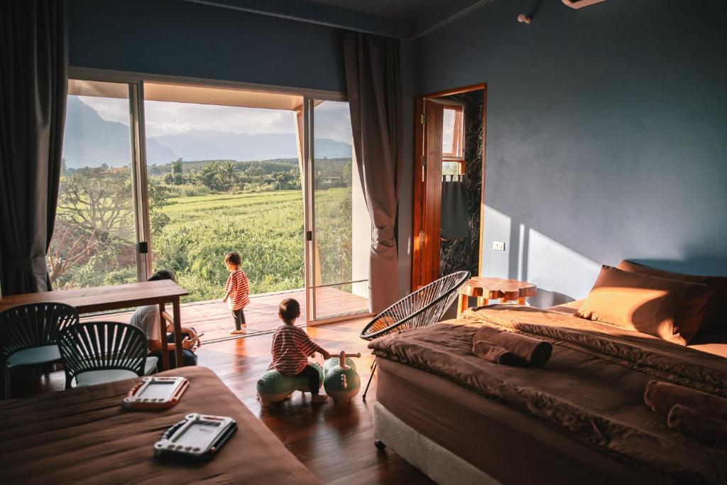 two children in a bedroom with a bed and a large window at Daraga ดารกะ in Chiang Dao