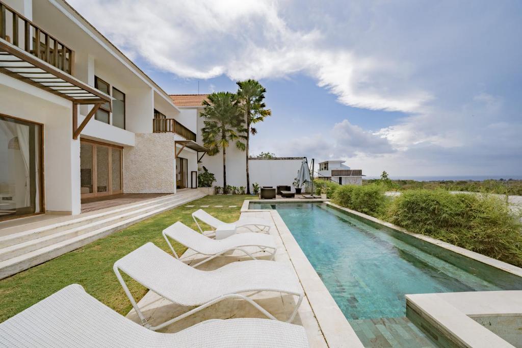 einen Pool mit weißen Liegestühlen neben einem Haus in der Unterkunft Mermaid Villa Bingin in Bingin Beach