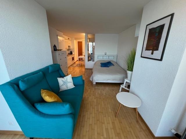 Una sala de estar con un sofá azul y una cama. en Studio avec accès direct au lac de Geneve, en Saint-Gingolph