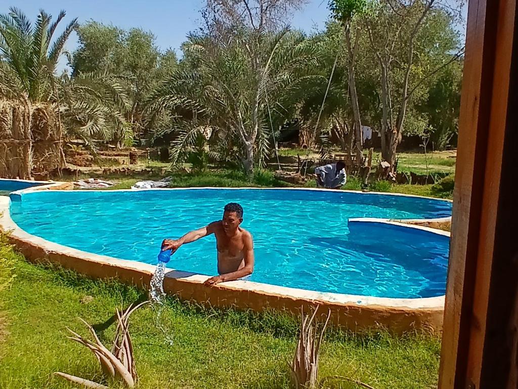 a man is pouring water into a swimming pool at The Green Siwa Hotel in Siwa