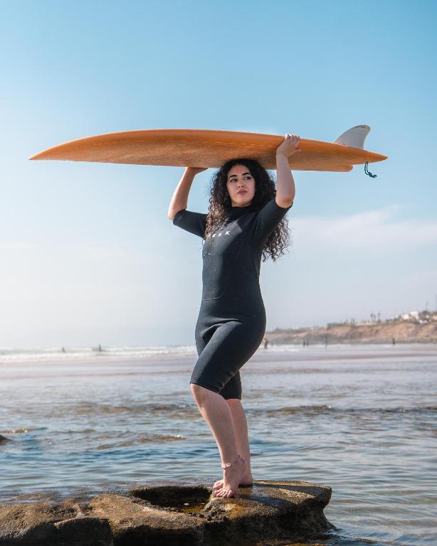 a woman standing on a rock holding a surfboard at Tayyurt Blue waves Beach house's in Oulad Akkou