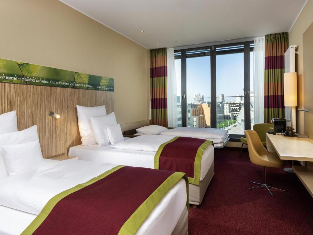 una camera d'albergo con due letti e una scrivania di Mövenpick Hotel Frankfurt City Messe a Francoforte sul Meno