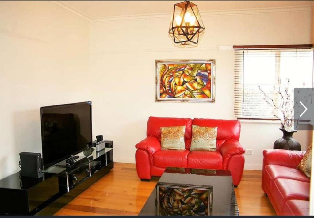 a living room with a red couch and a tv at Comfy & Budget-Friendly Home in Balwyn - Quiet & Close to Melbourne CBD in Balwyn