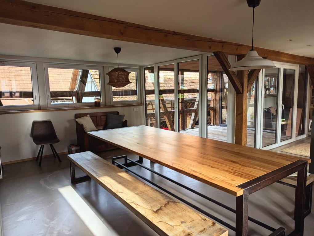 un grande tavolo in legno in una stanza con finestre di L'Étable - à l'Ancienne Ferme 