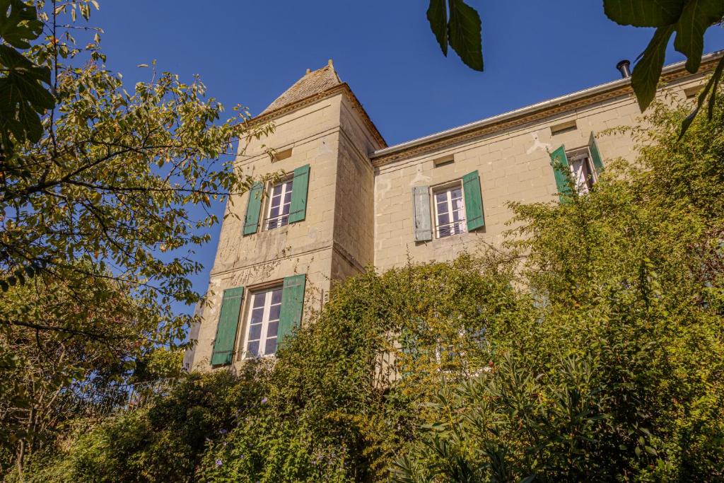 a building with green shuttered windows and trees at Castel La Fabrik'Créative in Saint-Barthélémy-dʼAgenais