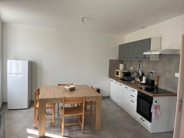 a kitchen with a wooden table and a white refrigerator at Appartement meublé tout équipé - Mesnard-La-Barotière in Mesnard-la-Barotière