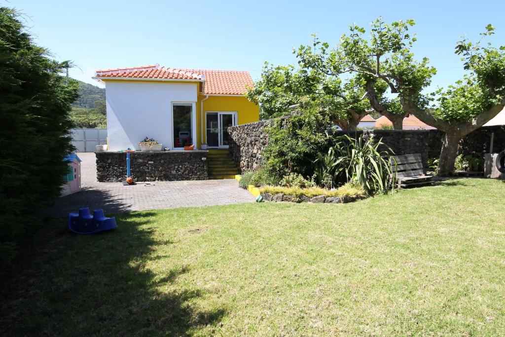 una pequeña casa amarilla con un patio con un árbol en Casa dos Biscoitos, en Praia da Vitória