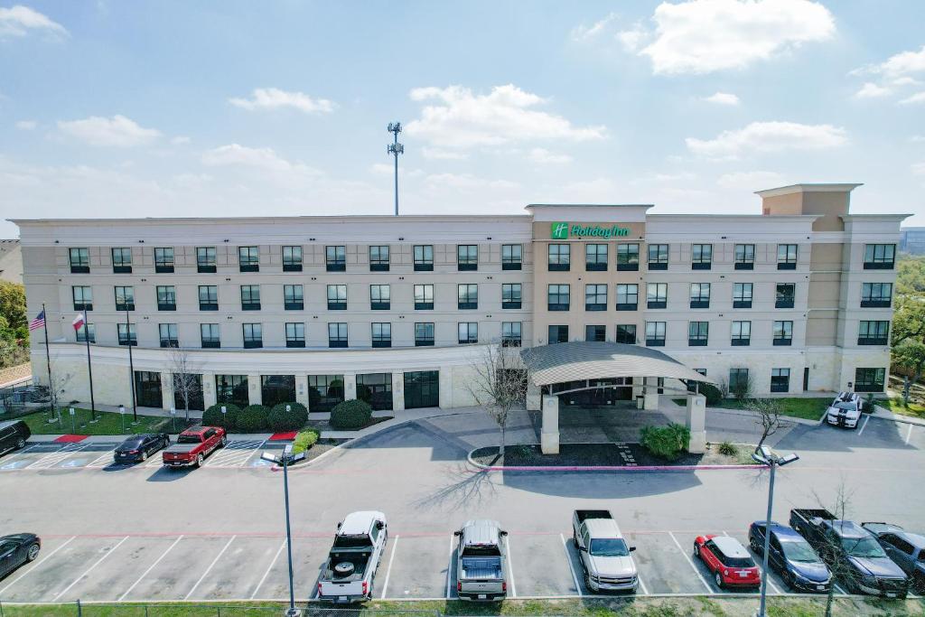 Hotel Holiday Inn San Antonio North Stone Oak Area by IHG-Newly Renovated, a large white building with cars parked in a parking lot at Holiday Inn San Antonio North Stone Oak Area by IHG-Newly Renovated in San Antonio