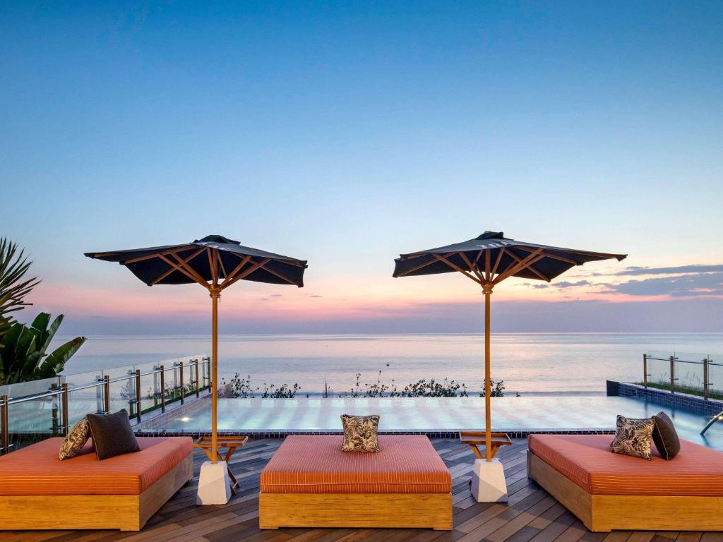 a deck with two beds and umbrellas and the ocean at Tribe Bali Kuta Beach in Kuta