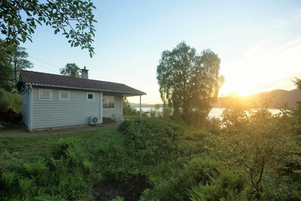a small house in a field with the sunset in the background at Beautiful panorama fjord wiew 40 min from Bergen in Hamre